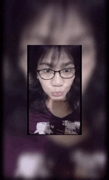 a woman wearing glasses and a purple shirt looks at the camera