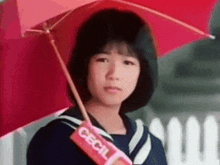 a young girl in a sailor suit is holding a red umbrella over her head .