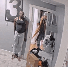 a man in a black tank top and white pants is standing in a room with a number 3 on the wall