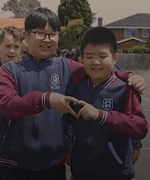 two boys wearing jackets with the letter m on them are making a heart with their hands