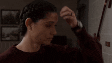 a woman in a maroon sweater is braiding her hair .