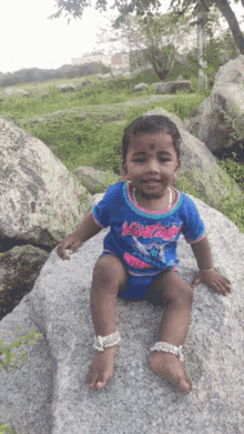a little boy is sitting on a rock wearing a blue shirt that says ' victoria ' on it