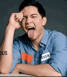 a man in a blue shirt is sticking his tongue out while sitting at a table .