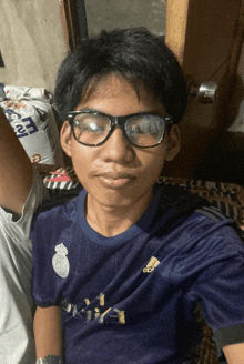 a man wearing glasses and a blue adidas shirt looks at the camera