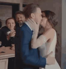 a bride and groom are kissing at their wedding reception while a group of people watch .
