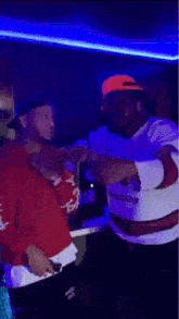 two men are standing next to each other in a dark room with neon lights .