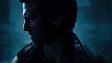 a man with a beard is standing in a dark room with red and blue lights behind him .