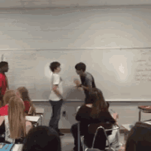 a group of students are standing in front of a white board in a classroom