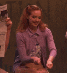 a woman in a purple sweater is smiling and holding a newspaper