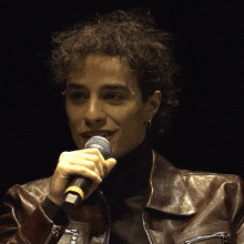a man in a leather jacket is holding a microphone and smiling