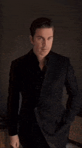 a man in a suit is standing in a dark room holding a coat over his shoulder