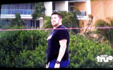 a man is standing in front of a building with the word true on the bottom right