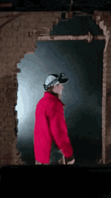 a man wearing a red jacket and goggles is walking through a hole in a brick wall