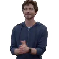 a man in a blue hoodie applauds with his hands together