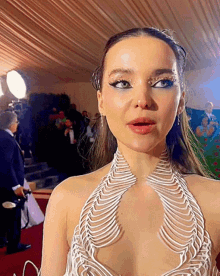 a woman in a white dress stands on a red carpet in front of a man holding a camera