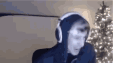 a man wearing headphones and a hoodie is standing in front of a christmas tree .