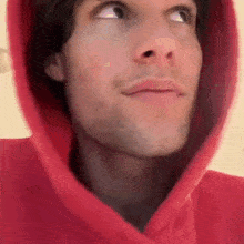 a close up of a man wearing a red hoodie with his eyes closed .