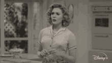 a woman is standing in a kitchen in a black and white photo from disney + .