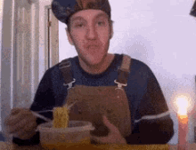 a man in overalls and a hat is eating noodles
