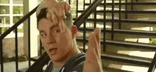 a man is sitting on a set of stairs with his hands up and a hand on his head .