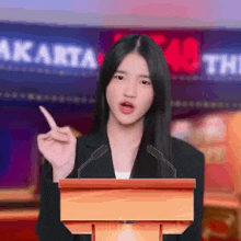 a young woman is standing at a podium giving a speech and pointing at something .