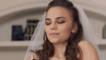 a bride in a wedding dress and veil with her eyes closed is smiling .