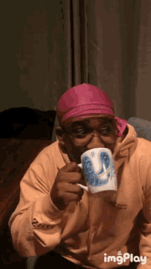 a man wearing a pink headband and glasses is drinking from a white mug