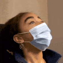 a woman wearing a face mask and earrings looks up at something