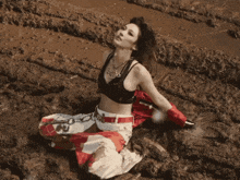 a woman in a black top and white pants is laying in the mud