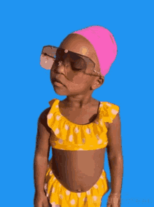 a little girl wearing a yellow bikini and sunglasses and a pink swim cap .