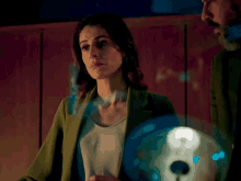 a woman in a green jacket stands in front of a light