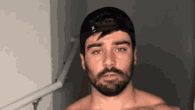 a shirtless man with a beard and a hat is standing in a dark room .
