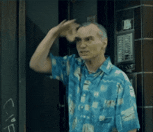a man in a blue shirt scratches his head in front of a door