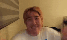 a man with red hair and a white shirt is smiling and waving at the camera .