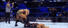 two women are wrestling in a ring with a referee in the background .