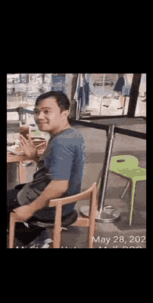 a man in a blue shirt is sitting in a chair holding a cup of coffee .