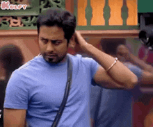 a man in a blue t-shirt is scratching his head while standing in front of a building .