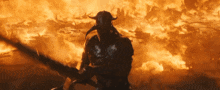 a man with horns is holding a sword in front of a large fire