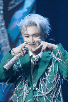 a man wearing a green jacket with chains around his arms makes a heart shape with his hands