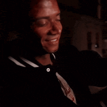 a man in a black shirt and tie is smiling in a dark room