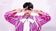 a young boy wearing a pink striped shirt and a white bow tie is making a peace sign with his hands .