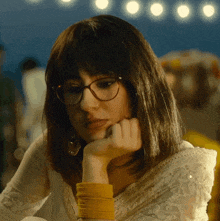 a woman wearing glasses and a yellow bracelet rests her hand on her chin