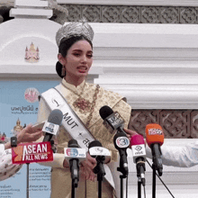 a woman wearing a crown and a sash that says mut stands in front of a bunch of microphones