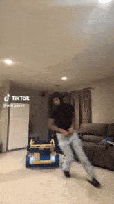 a man is dancing in a living room with a toy car in the background .