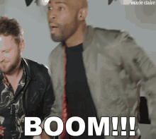 a man in a bomber jacket says boom while another man looks on