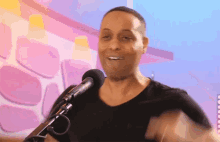 a man in a black shirt is singing into a microphone in front of a pink wall