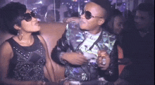 a man and a woman are sitting on a couch in a club . the woman is wearing sunglasses .