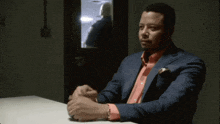 a man in a suit and a pink shirt sits at a table