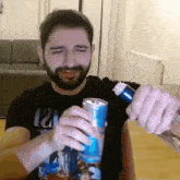 a man with a beard wearing a black shirt with the number 12 on it opens a can of soda