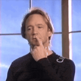a man in a black shirt with the letter c on the sleeve holds his finger to his mouth